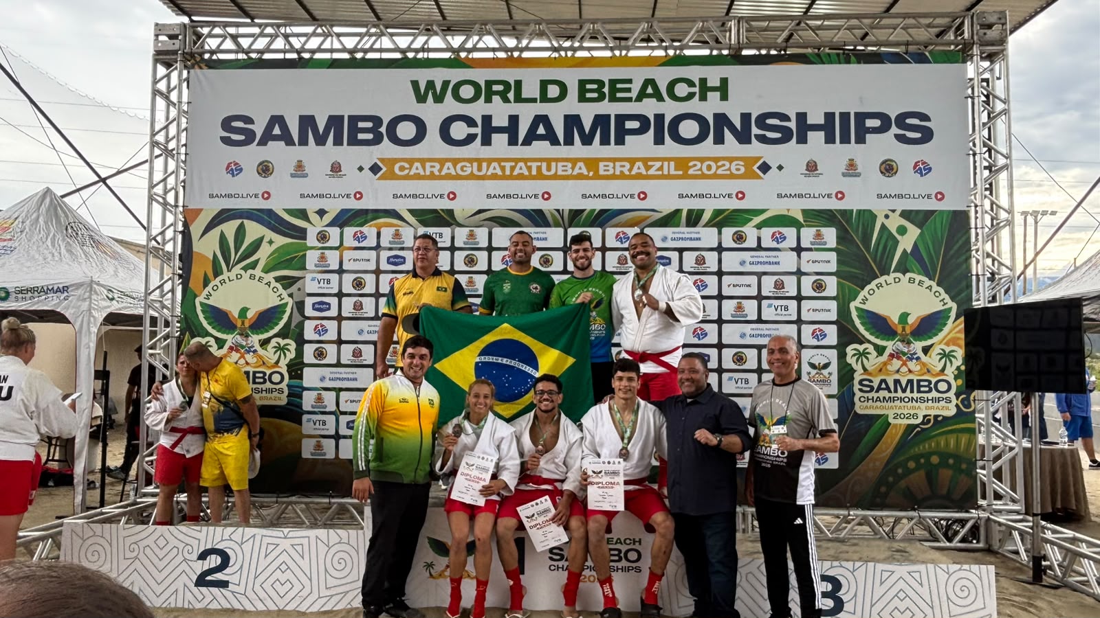 Equipe brasileira comemora no pódio do Mundial de Sambo de Praia 2026 com a bandeira do Brasil
